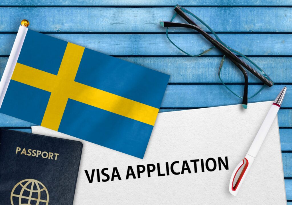 Flag of Sweden with a passport, a paper with visa application written on it, a pen and a pair of glasses