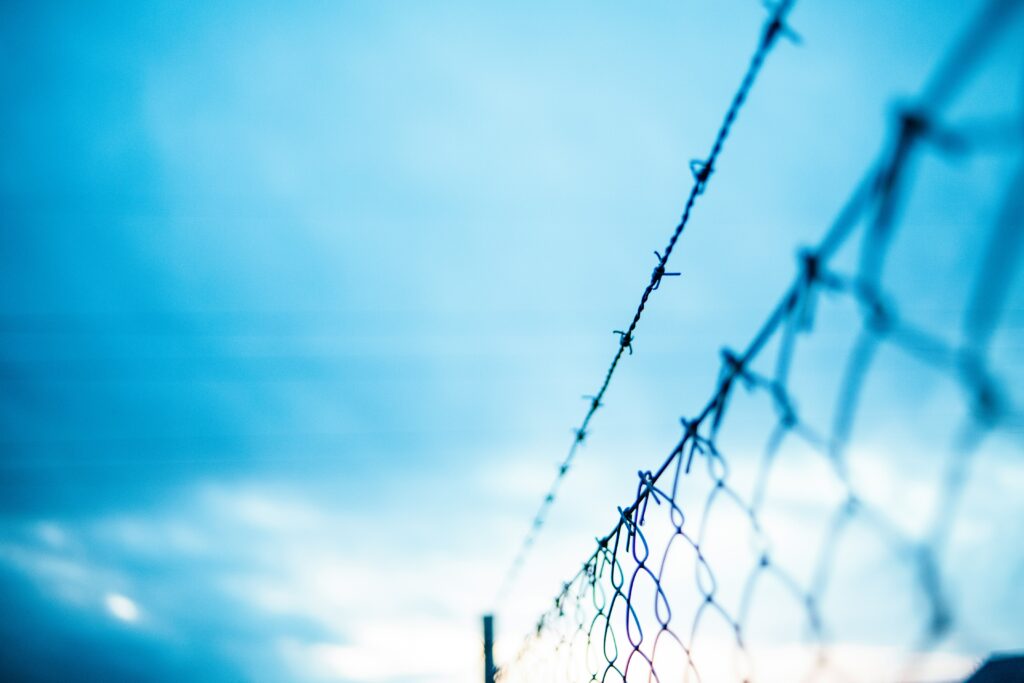 Barbed wire fence against a blue sky, symbolizing security and barriers.